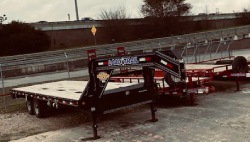 A bunch of utility trailers that are sitting in an enclosed lot next to a road