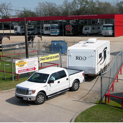 A white pickup truck towing a camper out of a fenced-in lot